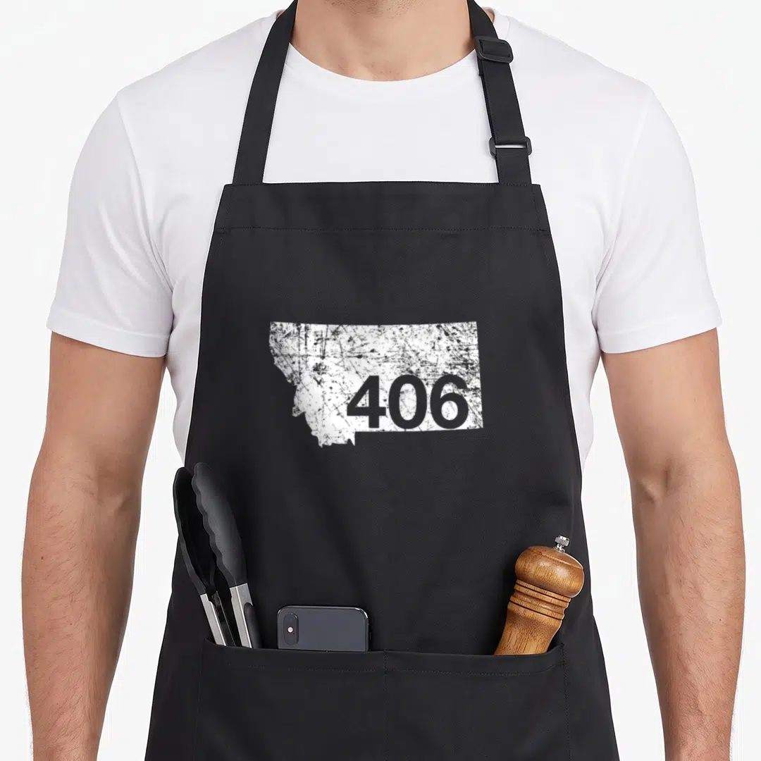 Montana area code apron - White distressed Montana state outline containing grey number 406 on grey background — shown on a black cotton canvas apron against a white background