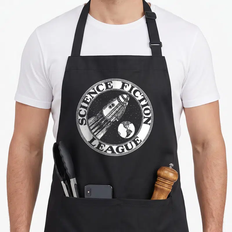 League science apron - Circular badge with rocket ship, planet, stars, and text SCIENCE FICTION LEAGUE in white line art — shown on a black cotton canvas apron against a white background