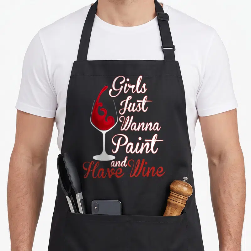 Wine sip and paint aprons - White wine glass with red splash and stacked text reading Girls Just Wanna Paint and Have — shown on a black cotton canvas apron against a white background