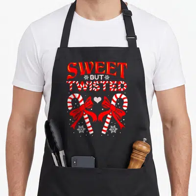 But candy cane apron - Stacked SWEET BUT TWISTED text above two red-bowed candy canes facing a pink heart among — shown on a black cotton canvas apron against a white background
