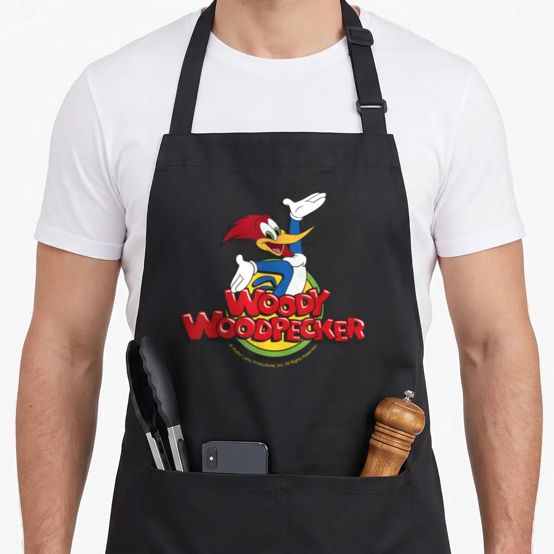 Funny woodpecker apron - Woody Woodpecker cartoon character in red and blue over yellow circle with red text — shown on a black cotton canvas apron against a white background