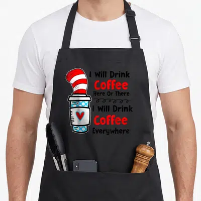Teaching drink teacher apron - Cartoon coffee cup with red white striped hat and text I Will Drink Coffee Here Or There — shown on a black cotton canvas apron against a white background