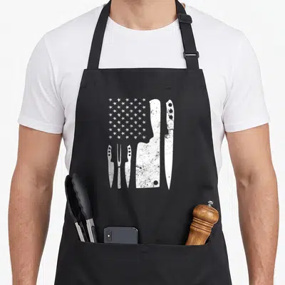 Knife 4th of july apron - Five white distressed knives and white stars arranged in a partial flag pattern on canvas — shown on a black cotton canvas apron against a white background