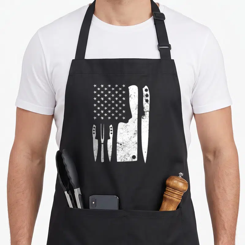 Knife 4th of july apron - Five white distressed knives and white stars arranged in a partial flag pattern on canvas — shown on a black cotton canvas apron against a white background