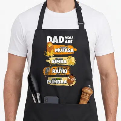 Stack lion dad apron - Vertical stack of Mufasa Simba Rafiki Pumbaa with white text on orange and yellow brushstrokes — shown on a black cotton canvas apron against a white background