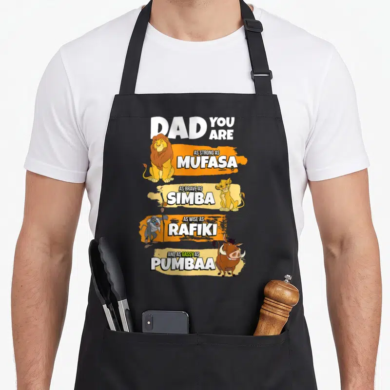 Stack lion dad apron - Vertical stack of Mufasa Simba Rafiki Pumbaa with white text on orange and yellow brushstrokes — shown on a black cotton canvas apron against a white background