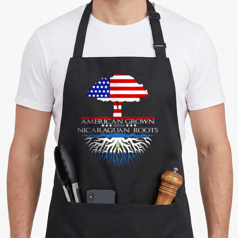 Caribbean american flag apron - Tree shaped like US flag above text American Grown With Nicaraguan Roots over roots — shown on a black cotton canvas apron against a white background