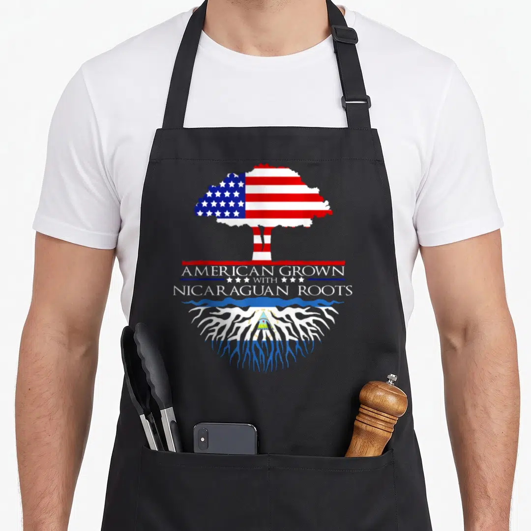 Caribbean american flag apron - Tree shaped like US flag above text American Grown With Nicaraguan Roots over roots — shown on a black cotton canvas apron against a white background