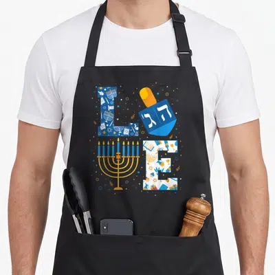 Hanukkah holiday christmas aprons - LOVE text formed by menorah, dreidel with Hebrew letters, and Hanukkah pattern — shown on a black cotton canvas apron against a white background
