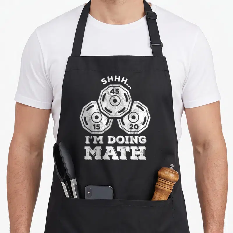 Shhh training apron - White weight plates 45 15 20 with SHHH I'M DOING MATH text — shown on a black cotton canvas apron against a white background