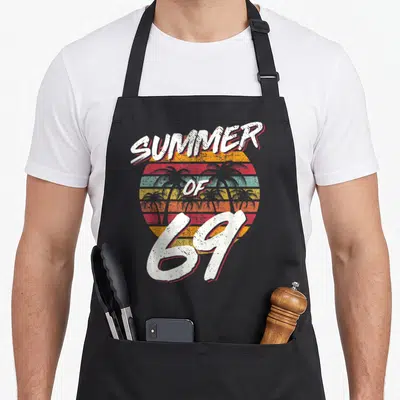55th daddy apron - Retro Summer of 69 striped sunset with palm tree silhouettes and distressed white lettering — shown on a black cotton canvas apron against a white background
