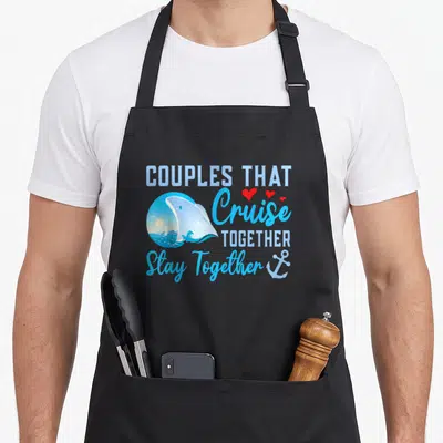 Lovely couple apron - Stacked blue text with ship vignette, three red hearts, and anchor — shown on a black cotton canvas apron against a white background