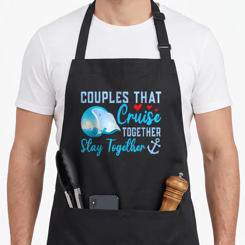 Lovely couple apron - Stacked blue text with ship vignette, three red hearts, and anchor — shown on a black cotton canvas apron against a white background
