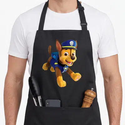 Funny chase birthday apron - Cartoon brown dog in blue hat and vest with yellow accents leaping forward — shown on a black cotton canvas apron against a white background