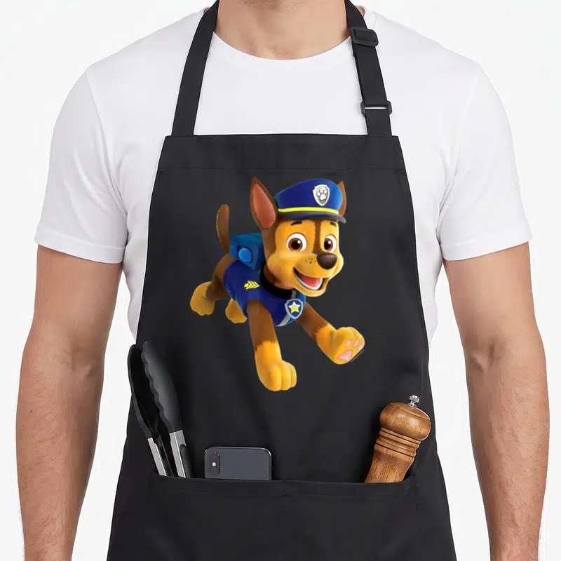 Funny chase birthday apron - Cartoon brown dog in blue hat and vest with yellow accents leaping forward — shown on a black cotton canvas apron against a white background