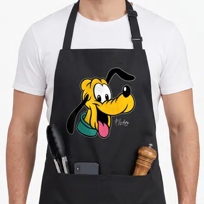 Pluto face apron - Cartoon dog head in yellow and teal with pink tongue and script text reading Pluto — shown on a black cotton canvas apron against a white background