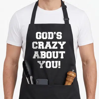 Cool god christian apron - White block letters spelling GOD'S CRAZY ABOUT YOU! stacked vertically — shown on a black cotton canvas apron against a white background
