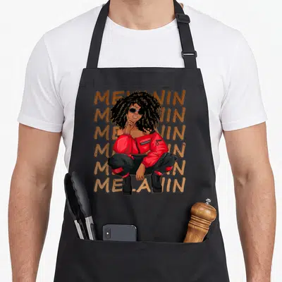 Melanin hair apron - Woman crouching in front of six stacked Melanin words in brown, red, and black — shown on a black cotton canvas apron against a white background