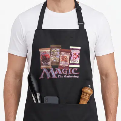Planeswalker magic apron - Four vintage Magic The Gathering booster packs and logo in purple, brown, and gold photo — shown on a black cotton canvas apron against a white background