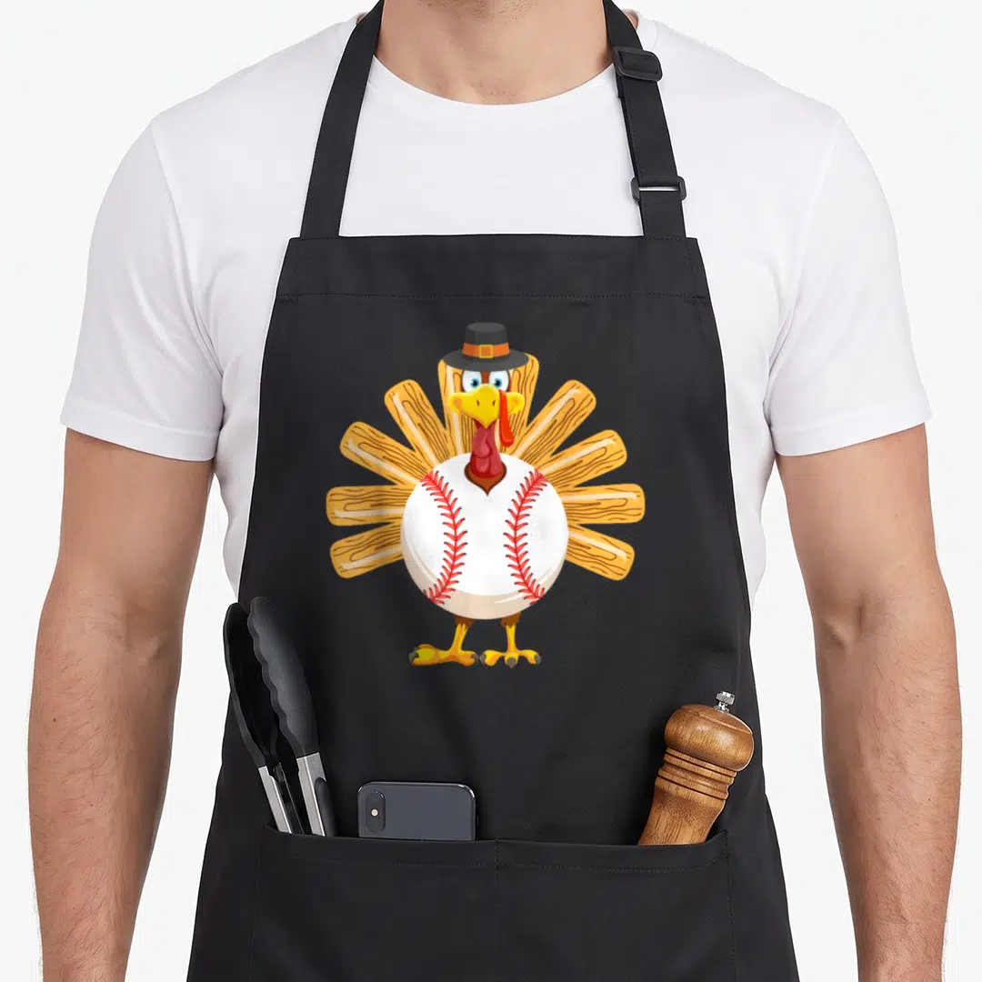 Baseball funny turkey apron - Cartoon turkey with baseball body, pilgrim hat, and fanned tail feathers in brown — shown on a black cotton canvas apron against a white background