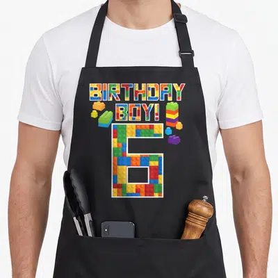 6th building aprons - BIRTHDAY BOY! 6 text filled with colorful plastic brick patterns and loose blocks — shown on a black cotton canvas apron against a white background
