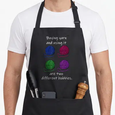 Buying knitting apron - Four yarn balls in blue, red, green, and purple arranged in a grid with white text above — shown on a black cotton canvas apron against a white background