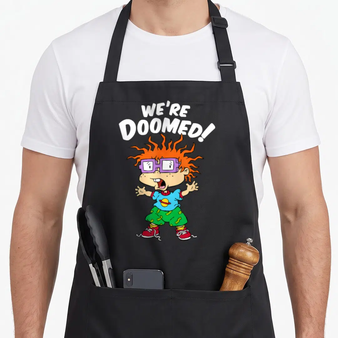 Doomed white apron - Cartoon boy with orange spiky hair and purple glasses under arched We're Doomed text — shown on a black cotton canvas apron against a white background
