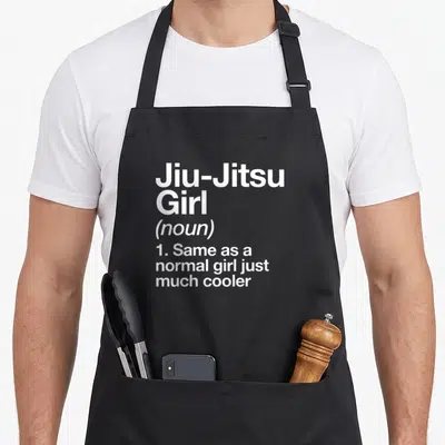 Jiu triangle apron - White stacked text reading Jiu-Jitsu Girl noun definition same as normal girl just much cooler — shown on a black cotton canvas apron against a white background