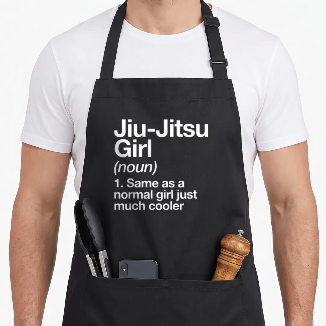 Jiu triangle apron - White stacked text reading Jiu-Jitsu Girl noun definition same as normal girl just much cooler — shown on a black cotton canvas apron against a white background