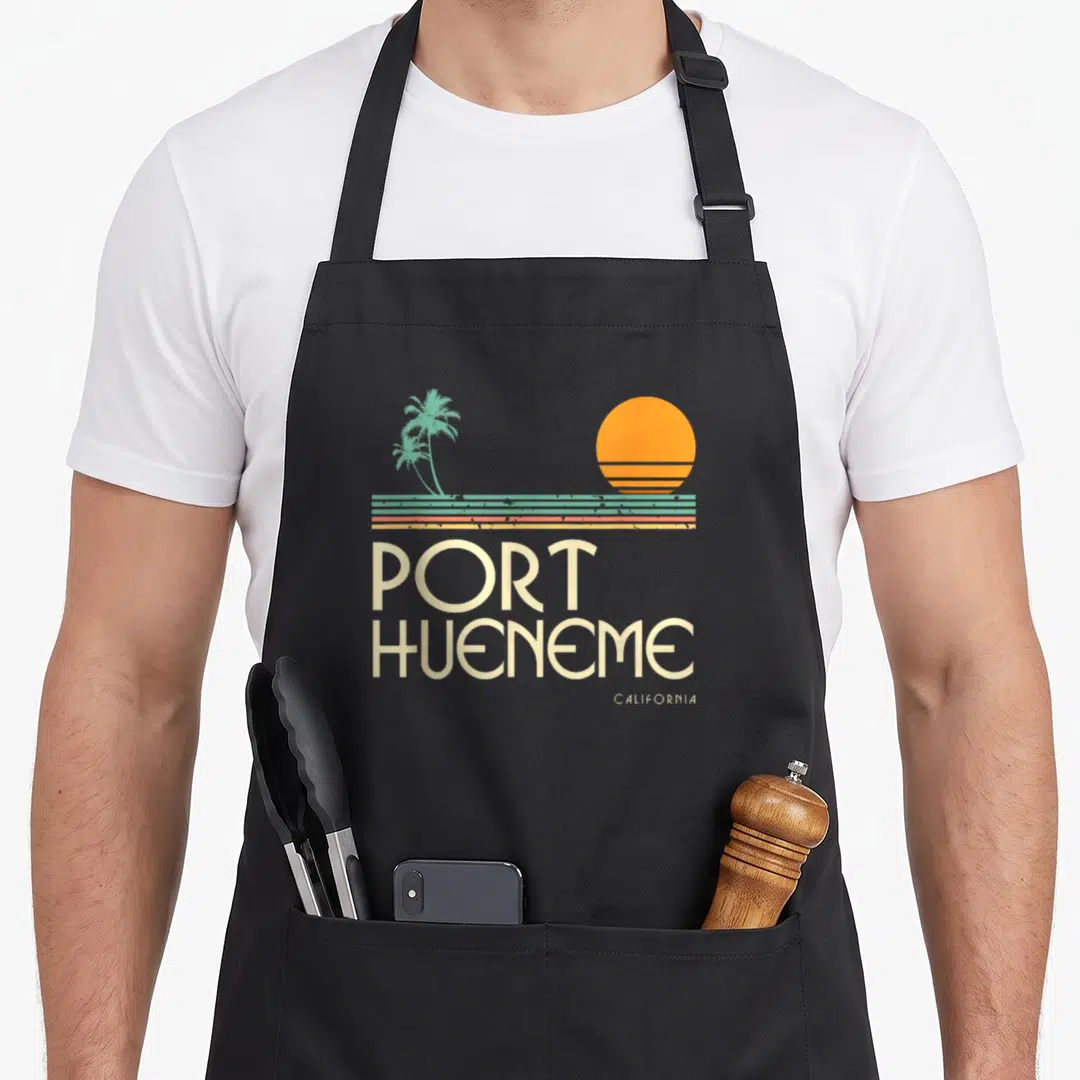 Hueneme vintage port apron - Retro sunset with teal lines and two palm trees above stacked beige PORT HUENEME — shown on a black cotton canvas apron against a white background