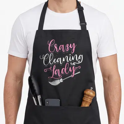 Vintage housekeeping housekeeper apron - Pink and white Crazy Cleaning Lady script with white broom lying horizontally — shown on a black cotton canvas apron against a white background