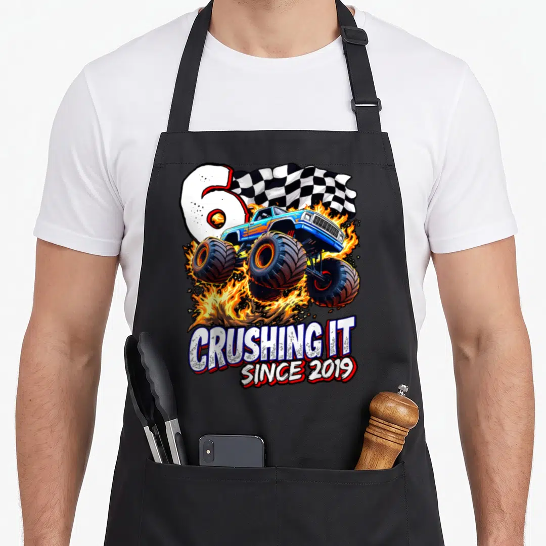 6th truck apron - Blue monster truck jumping through fire with number 6 and CRUSHING IT SINCE 2019 text — shown on a black cotton canvas apron against a white background