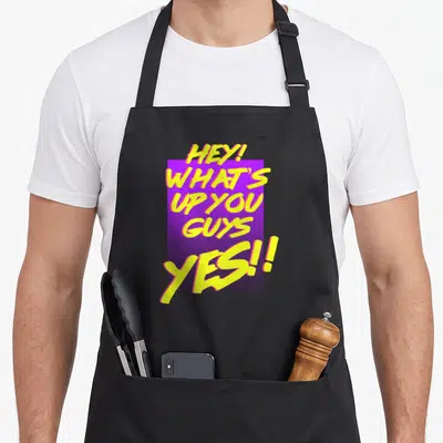 Dawson hey novelty apron - Yellow brush script text HEY WHATS UP YOU GUYS YES over purple rectangle — shown on a black cotton canvas apron against a white background