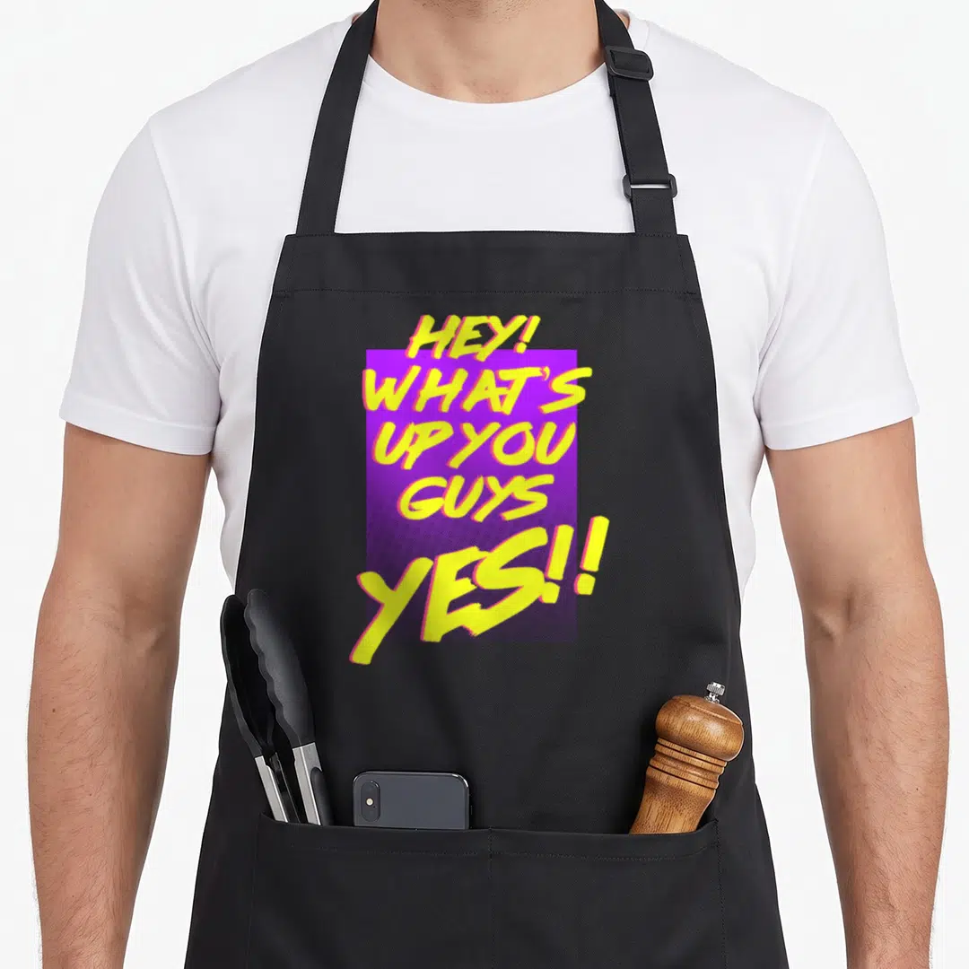 Dawson hey novelty apron - Yellow brush script text HEY WHATS UP YOU GUYS YES over purple rectangle — shown on a black cotton canvas apron against a white background