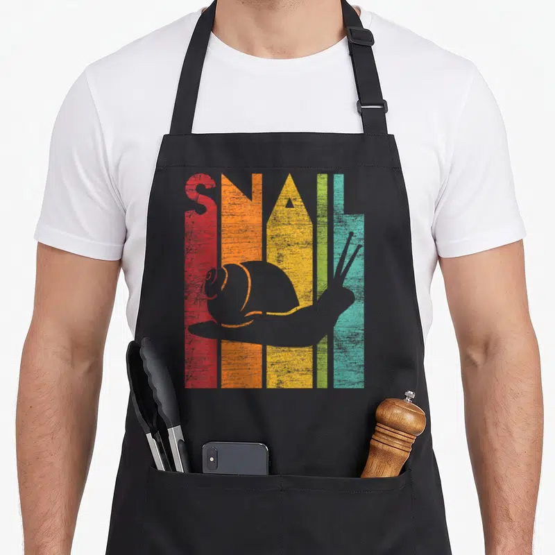Funny snail animal apron - Grey snail silhouette over five vertical colored stripes spelling SNAIL in red orange yellow — shown on a black cotton canvas apron against a white background