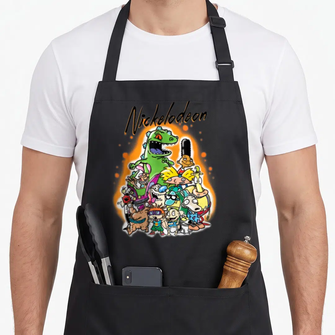 Nick urban apron - Arched Nickelodeon text above a cluster of cartoon characters on a glowing orange background — shown on a black cotton canvas apron against a white background