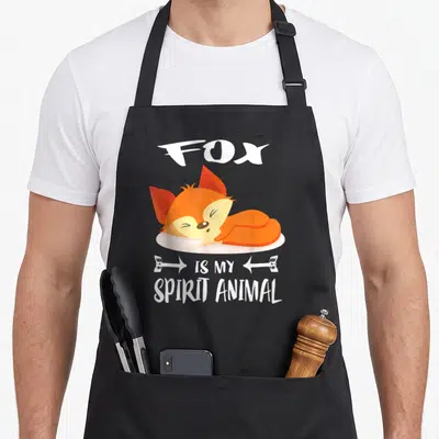 Animal fox aprons - Orange cartoon fox sleeping on pillow with white text reading Fox Is My Spirit Animal — shown on a black cotton canvas apron against a white background