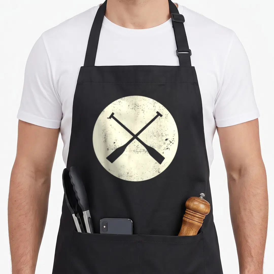 Paddle canoe apron - Two grey oars crossed in X shape inside distressed off-white circle — shown on a black cotton canvas apron against a white background