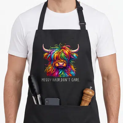 Hair highland cow apron - Multicolored cartoon highland cow head with text MESSY HAIR DON'T CARE below — shown on a black cotton canvas apron against a white background