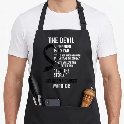 Melanoma devil's apron - Black awareness ribbon and white text reading The Devil Whispered In My Ear Melanoma Cancer — shown on a black cotton canvas apron against a white background
