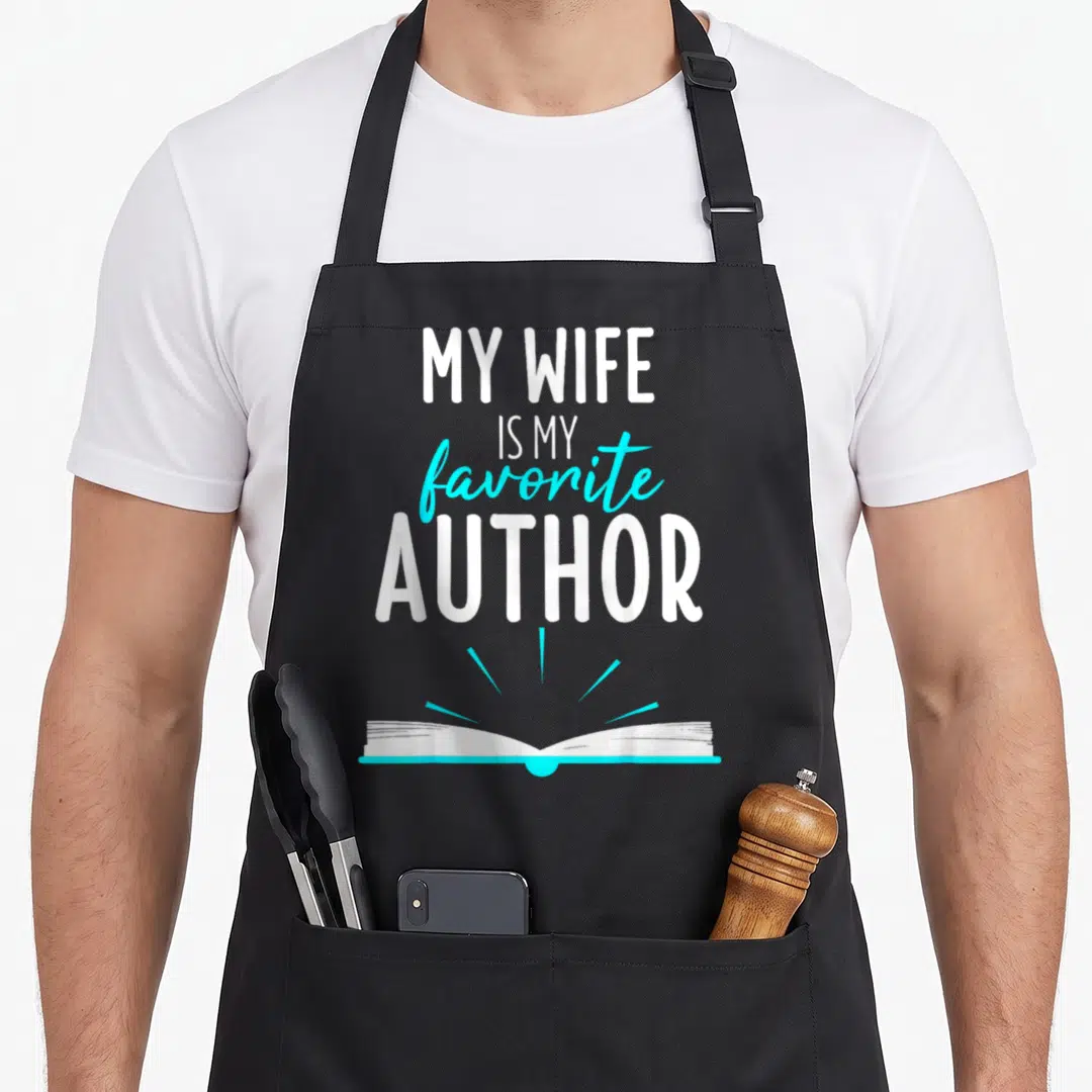 Author wife apron - Stacked white and cyan text My Wife Is My Favorite Author above a glowing open book — shown on a black cotton canvas apron against a white background