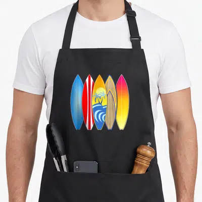 Surfboard surfing apron - Five cartoon surfboards in blue, red, yellow, pink, and brown; center board has palm tree — shown on a black cotton canvas apron against a white background