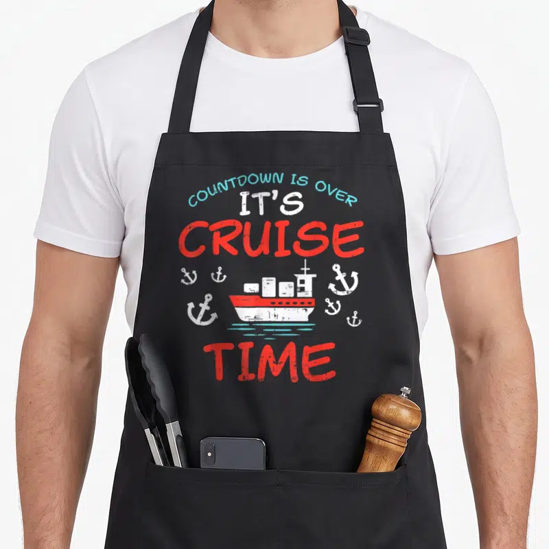 Ship countdown apron - Cruise ship and anchors with arched text COUNTDOWN IS OVER IT'S CRUISE TIME in red white and blue — shown on a black cotton canvas apron against a white background