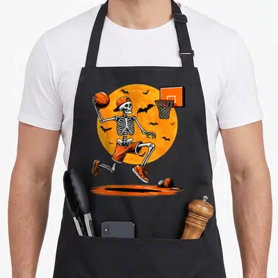 Basketball skeleton halloween apron - Cartoon skeleton in orange gear jumping with basketball near hoop and bats — shown on a black cotton canvas apron against a white background