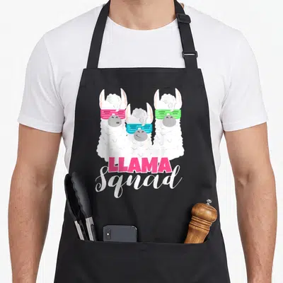 Llama 80s apron - Three cartoon llamas with pink blue and green sunglasses above pink and white stacked text — shown on a black cotton canvas apron against a white background