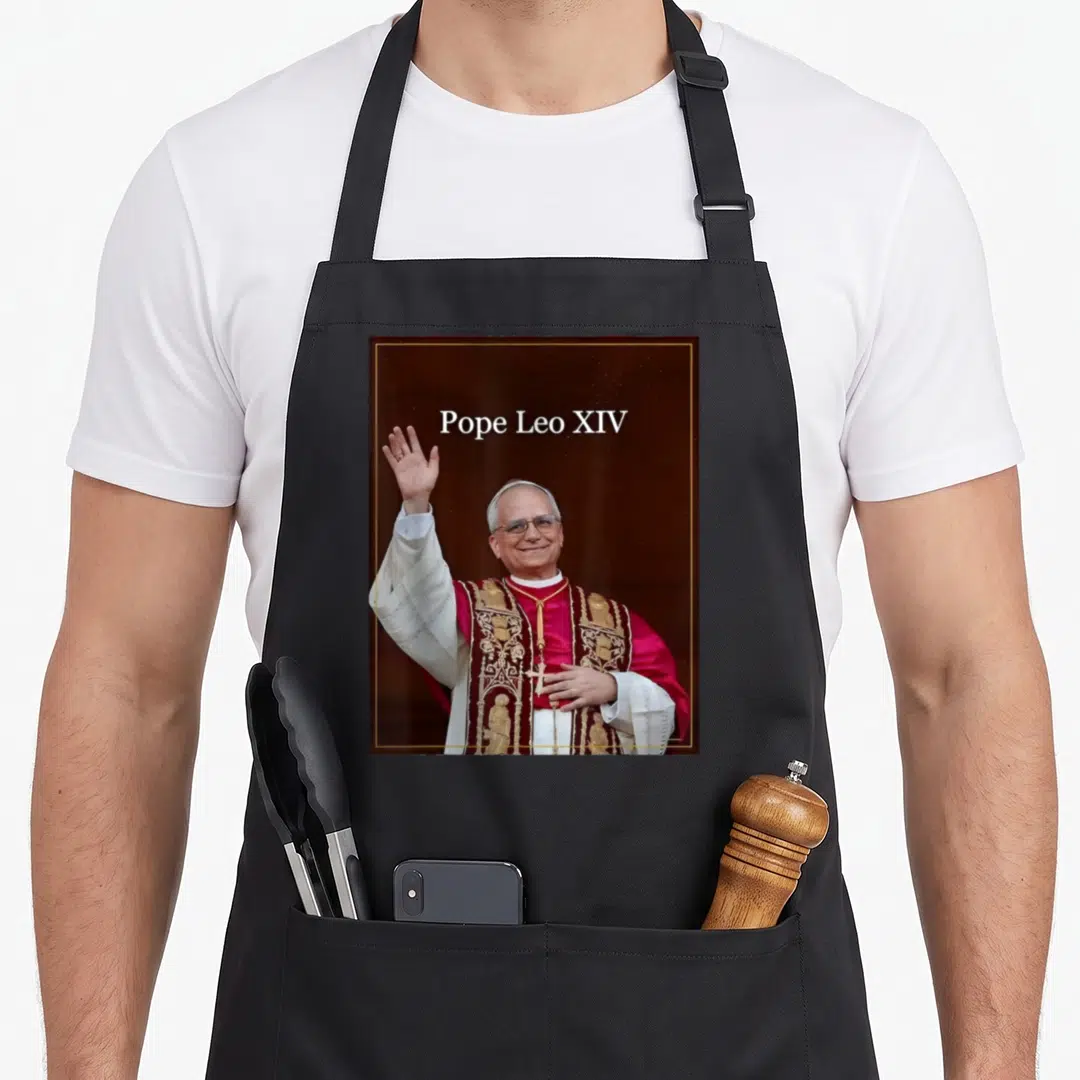 Pope leo apron - Photo of Pope Leo XIV waving in red and gold robes with white text above — shown on a black cotton canvas apron against a white background