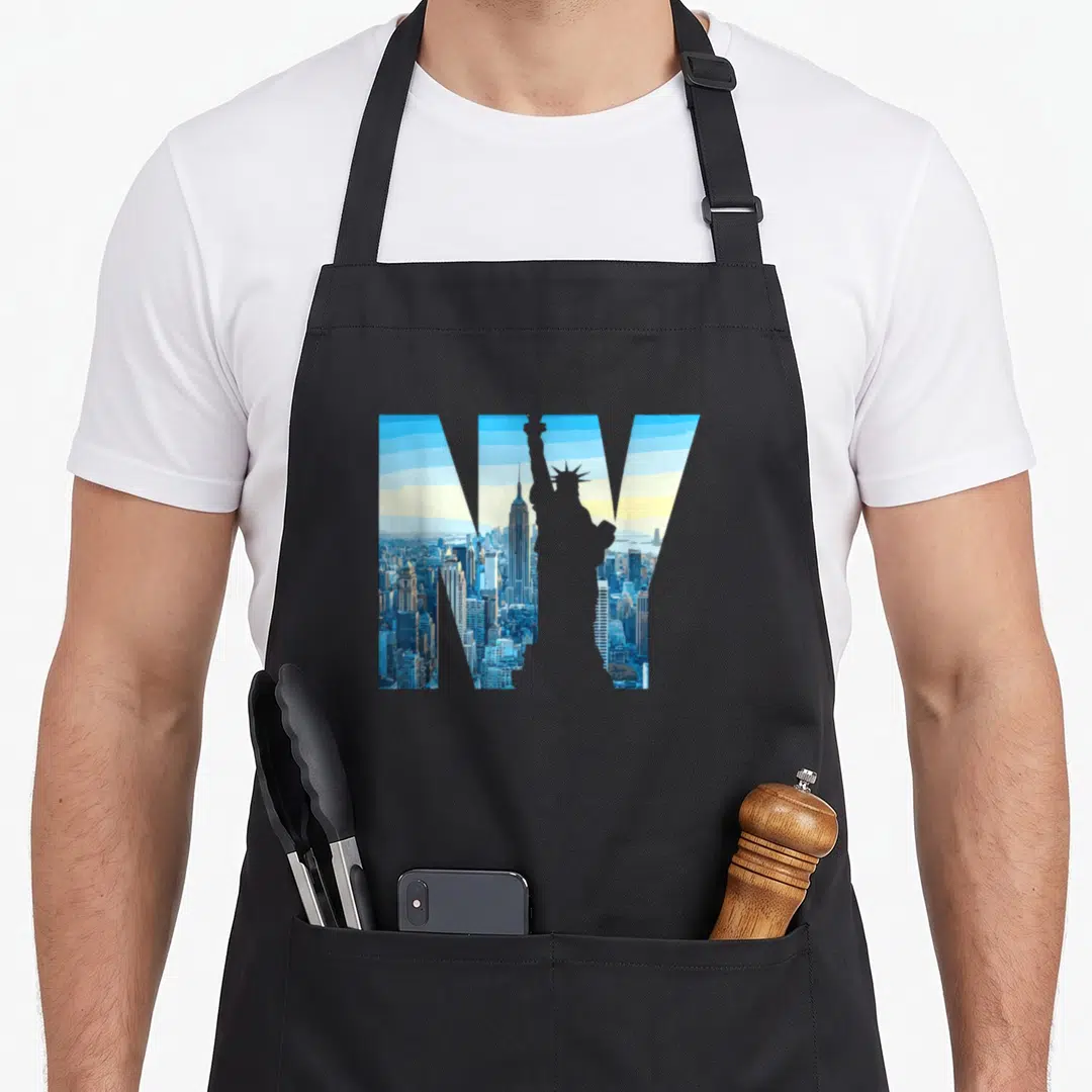 Nyc statue new york apron - NY letters filled with blue NYC skyline and grey Statue of Liberty silhouette — shown on a black cotton canvas apron against a white background