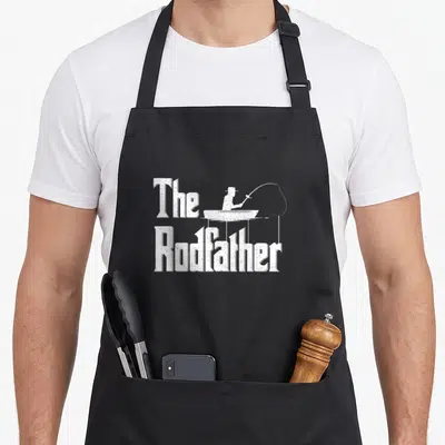 Funny rodfather fishing apron - Distressed white The Rodfather text with fisherman silhouette in a boat — shown on a black cotton canvas apron against a white background