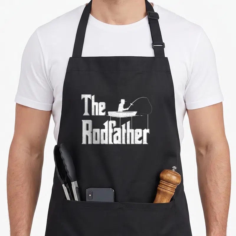 Funny rodfather fishing apron - Distressed white The Rodfather text with fisherman silhouette in a boat — shown on a black cotton canvas apron against a white background