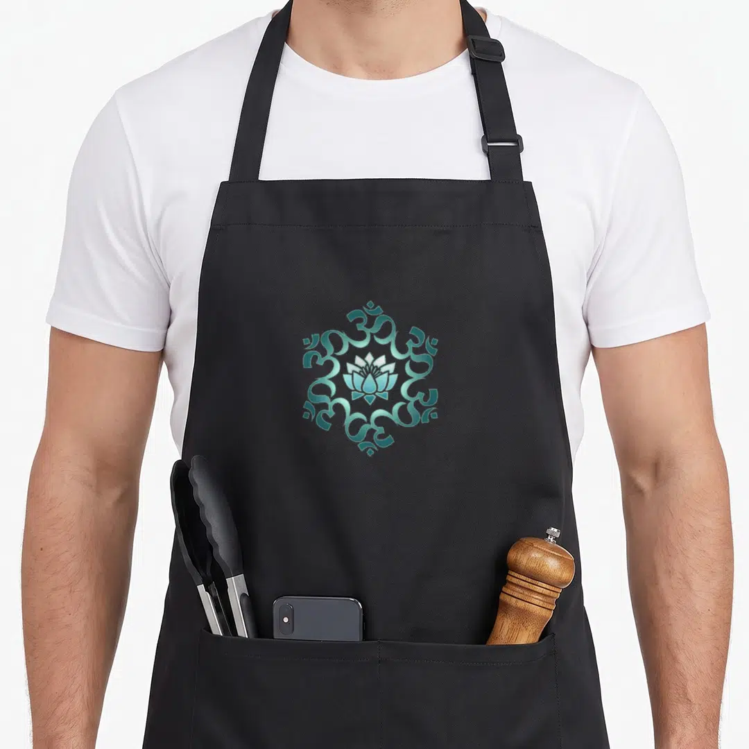 Mantra om symbol apron - Teal lotus flower surrounded by six Om symbols in a circular mandala pattern — shown on a black cotton canvas apron against a white background
